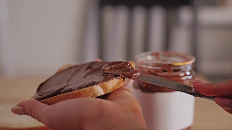 Slow motion captures woman spreading hazelnut chocolate cream onto white bread
