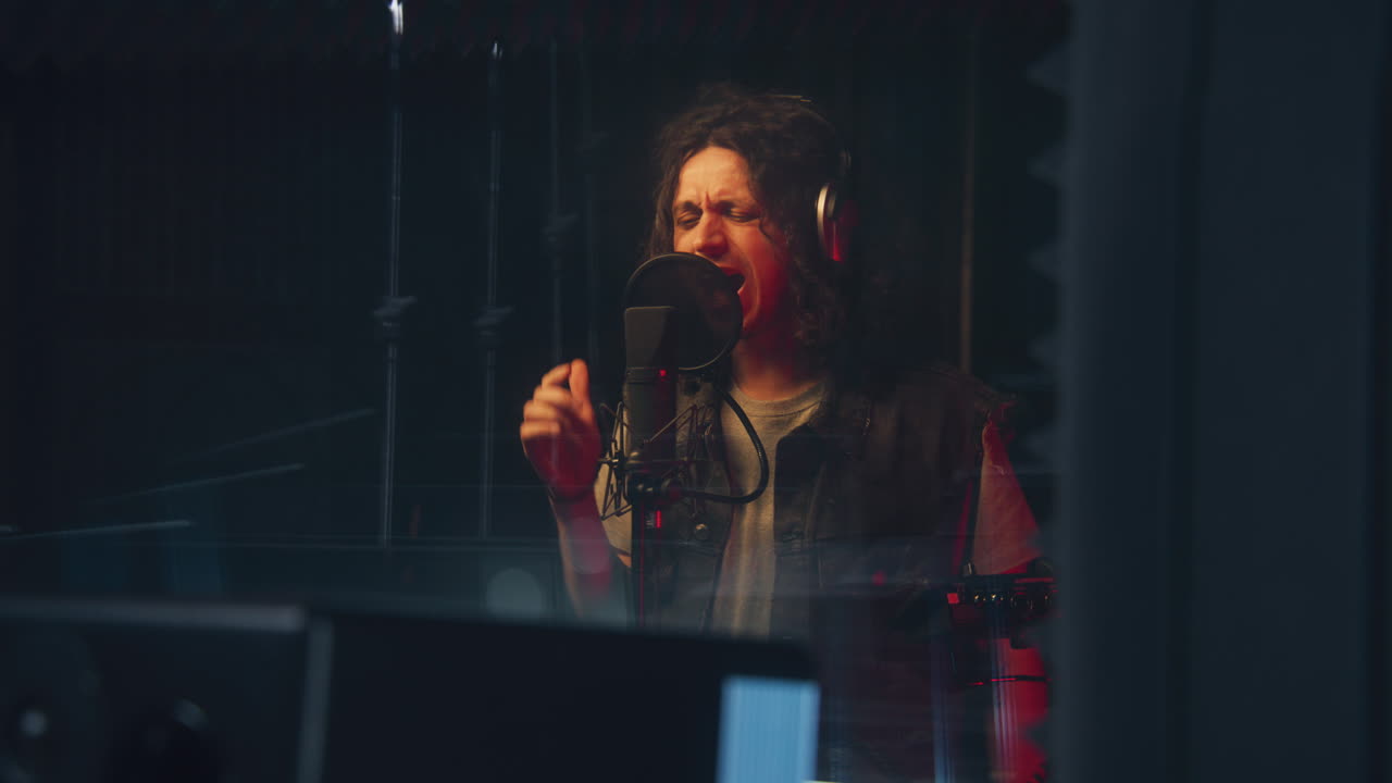 cantante masculino, artista, intérprete graba una nueva canción en una habitación a prueba de sonido. músico con auriculares canta en el micrófono profesional. equipo moderno de estudio de grabación de sonido. concepto de producción musical.