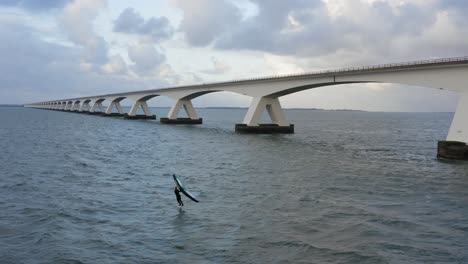 aerial scenic backward shot of a man wing surfing wind foiling near the de zeelandbrug longest bridge in holland