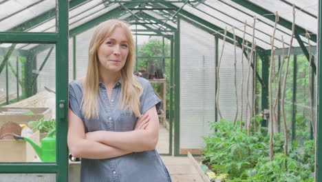 retrato de una mujer cultivando verduras de pie en la puerta del invernadero y doblando los brazos