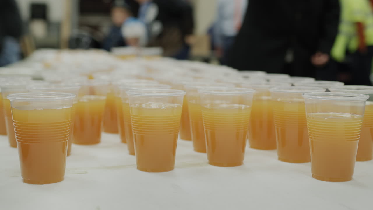 사람들은 테이블에서 플라스틱 컵으로 음료를 마시고 자원봉사자들은 사람들을 가열하고 음식으로 치료합니다.