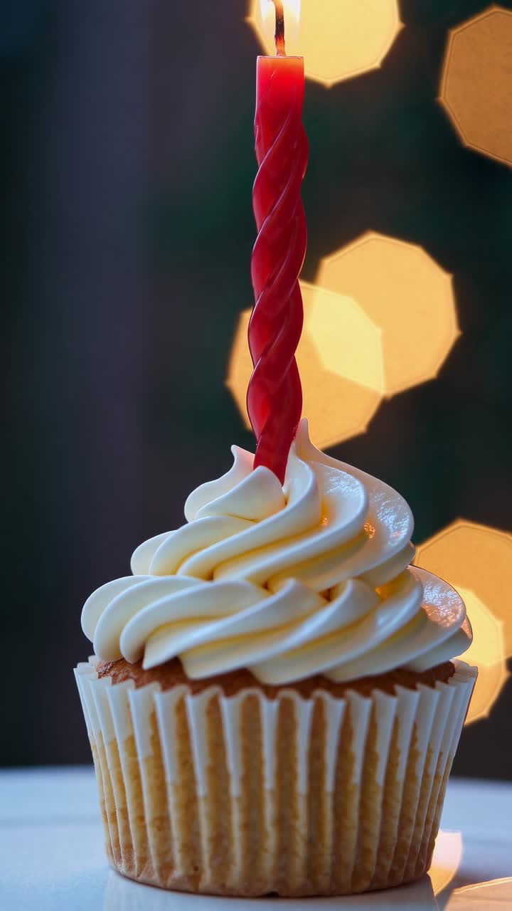 Primo piano di un cupcake con una candela rossa, scattata a livello degli occhi. Luci bokeh soffuse sullo sfondo.