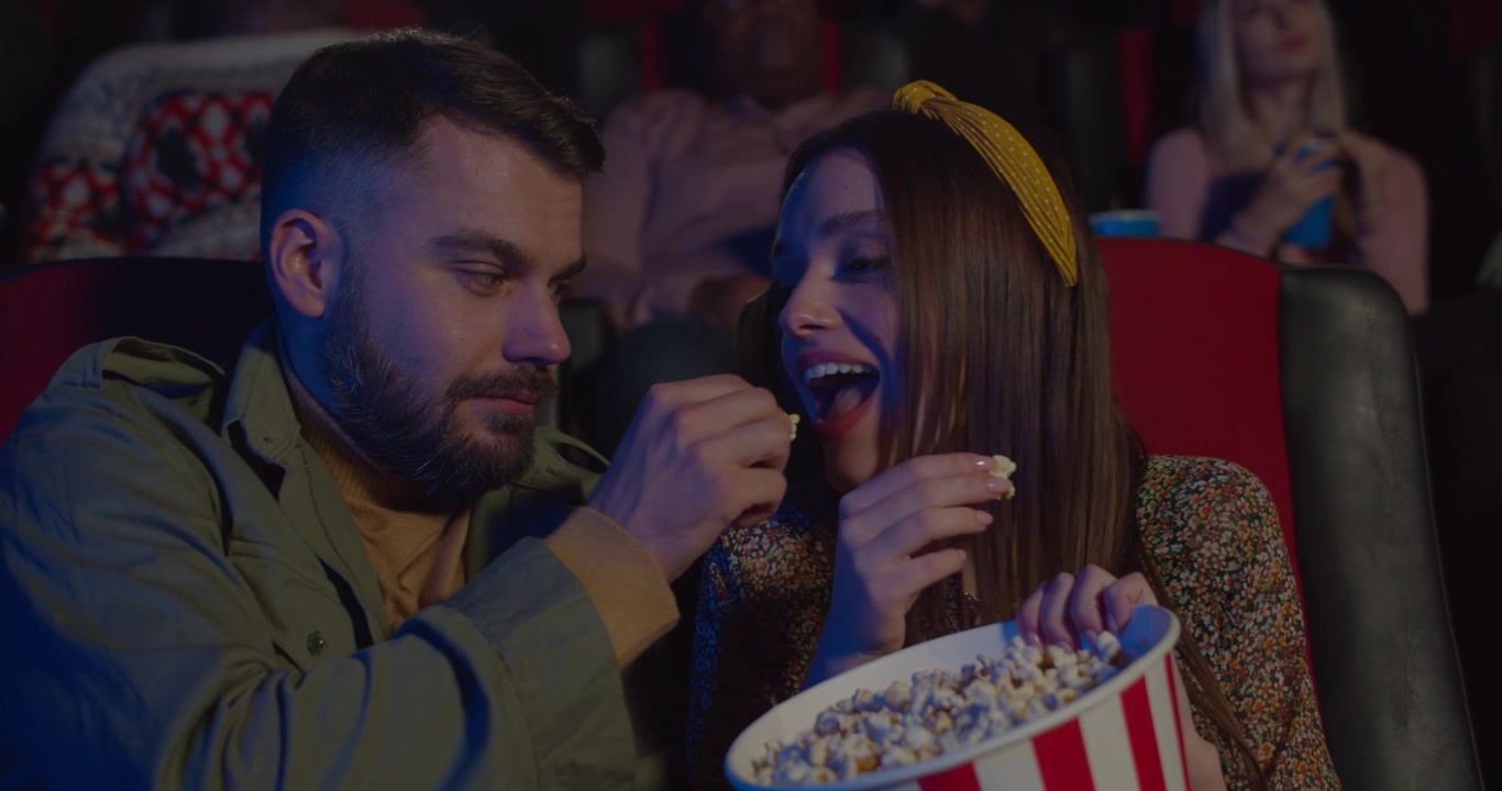 Giovane coppia che mangia popcorn mentre guarda un film al cinema.