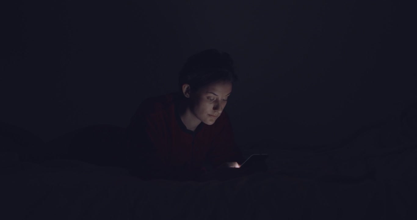 Kvinde bruger telefon i sengen om natten