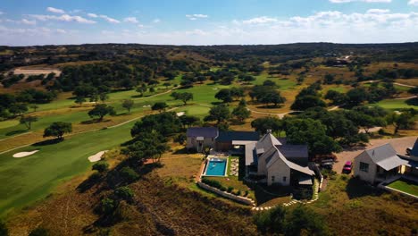 Mansión-En-La-Colina-Con-Vista-Al-Campo-De-Golf-Vuelo-Aéreo-Ver-órbita-Con-Gente-En-La-Piscina-En-Un-Día-Soleado-Con-Cielo-Azul-En-El-Club-De-Campo-De-Texas