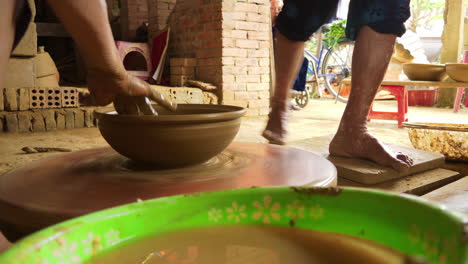 a close-up shot of traditional vietnam pottery turning on a foot-operated manual table, with clay and water in the foreground