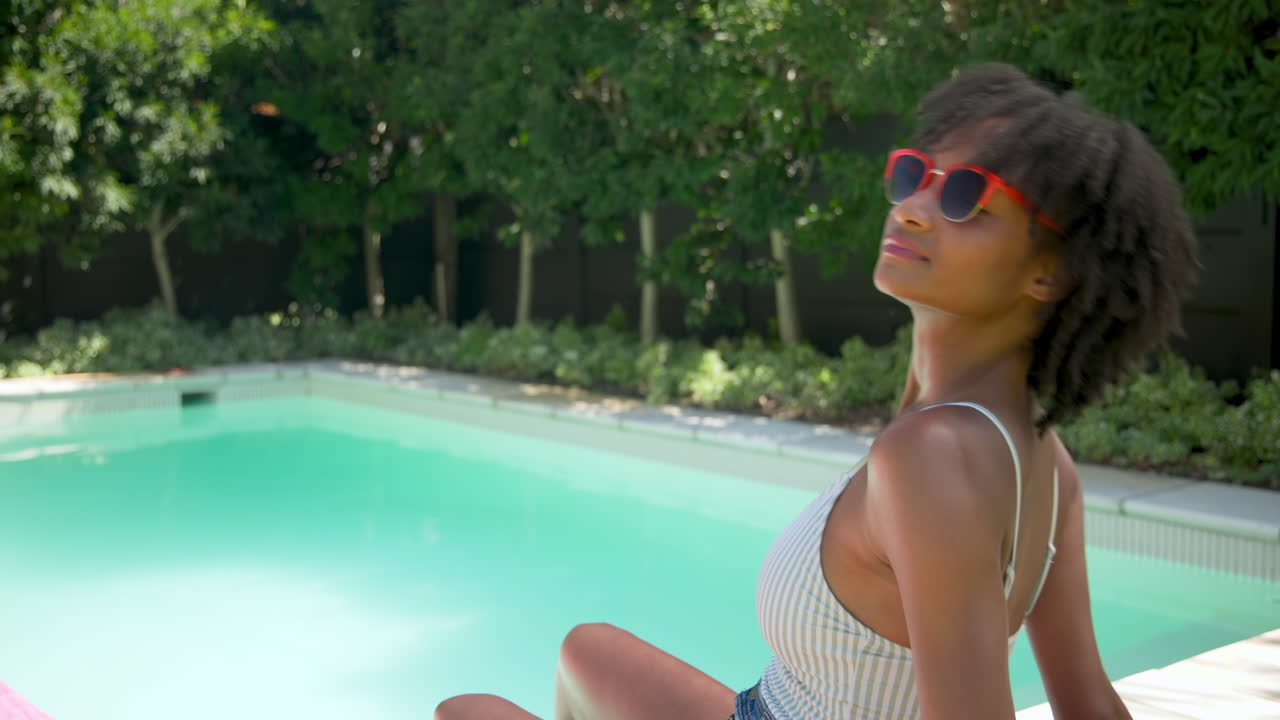 Relaxing by pool, woman in sunglasses enjoying sunny day with refreshing drink