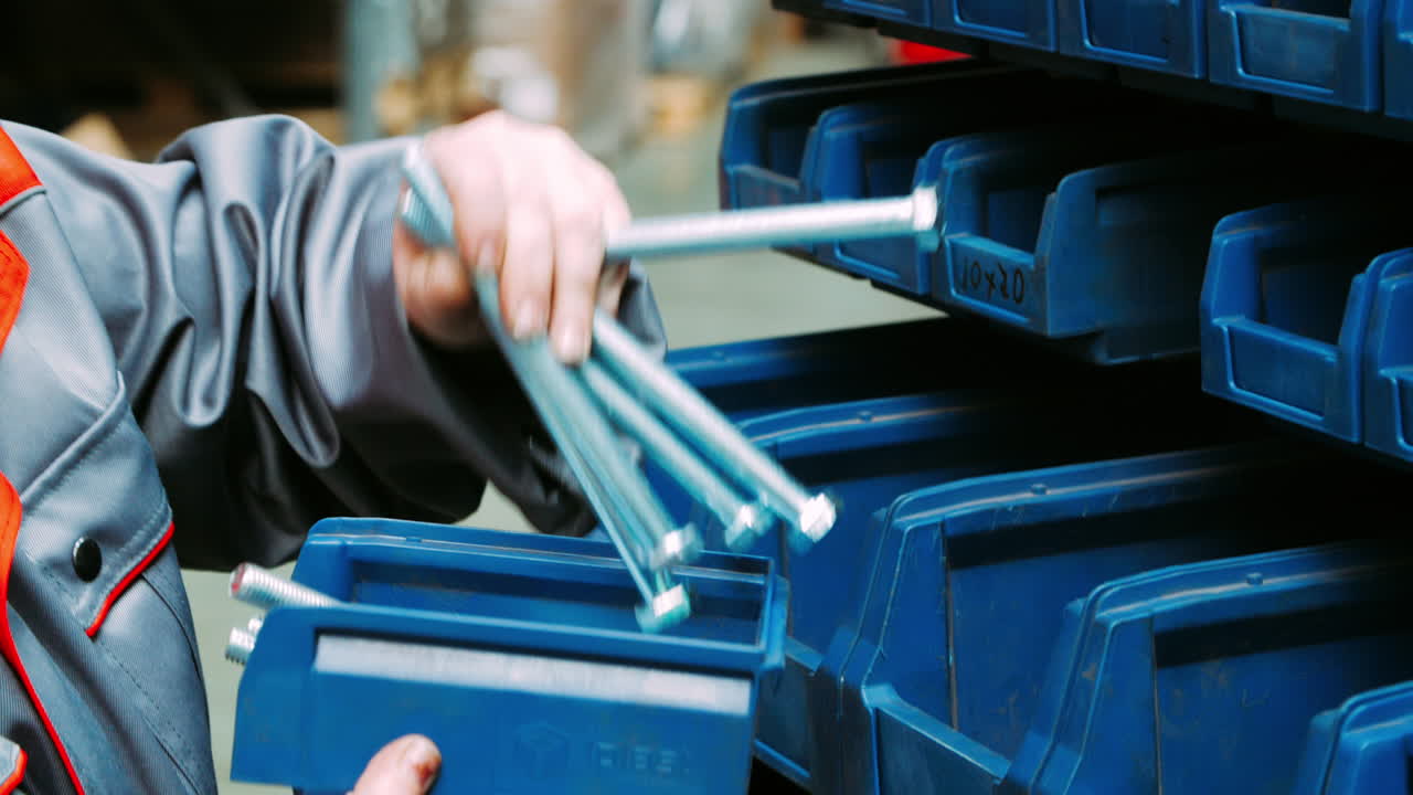 trabajador que almacena pernos largos en un compartimento de plástico. productos terminados