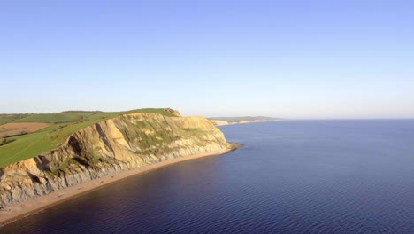 una amplia toma de imágenes aéreas de drones moviéndose sobre el mar vacío hacia la costa sur de inglaterra en una brillante noche soleada en la hora dorada.