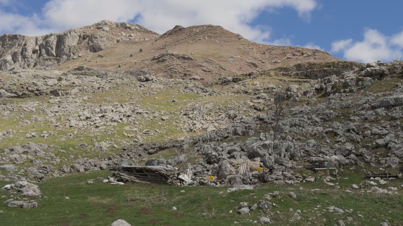 Una vista panoramica di montagna ripresa da un'auto in movimento, che mostra un paesaggio aspro di terreno roccioso e campi ricoperti di erba bassa. Giornata di sole, slow motion.