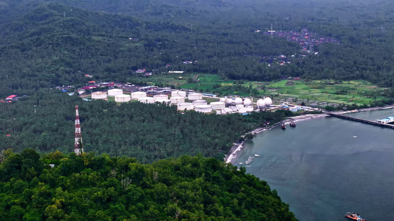 Pertamina TBBM Manggis, Bali’nin drone ile havadan çekilmiş görüntüsü – beyaz depolama tankları ve ormanlık tepelerin yanındaki iskele ile sakin koyu içeren kıyı yakıt terminali