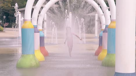 little girl runs under colorful water jets arches in park