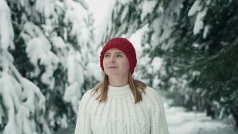 Caucasian-woman-wearing-red-hat-walking-in-snowing-forest.