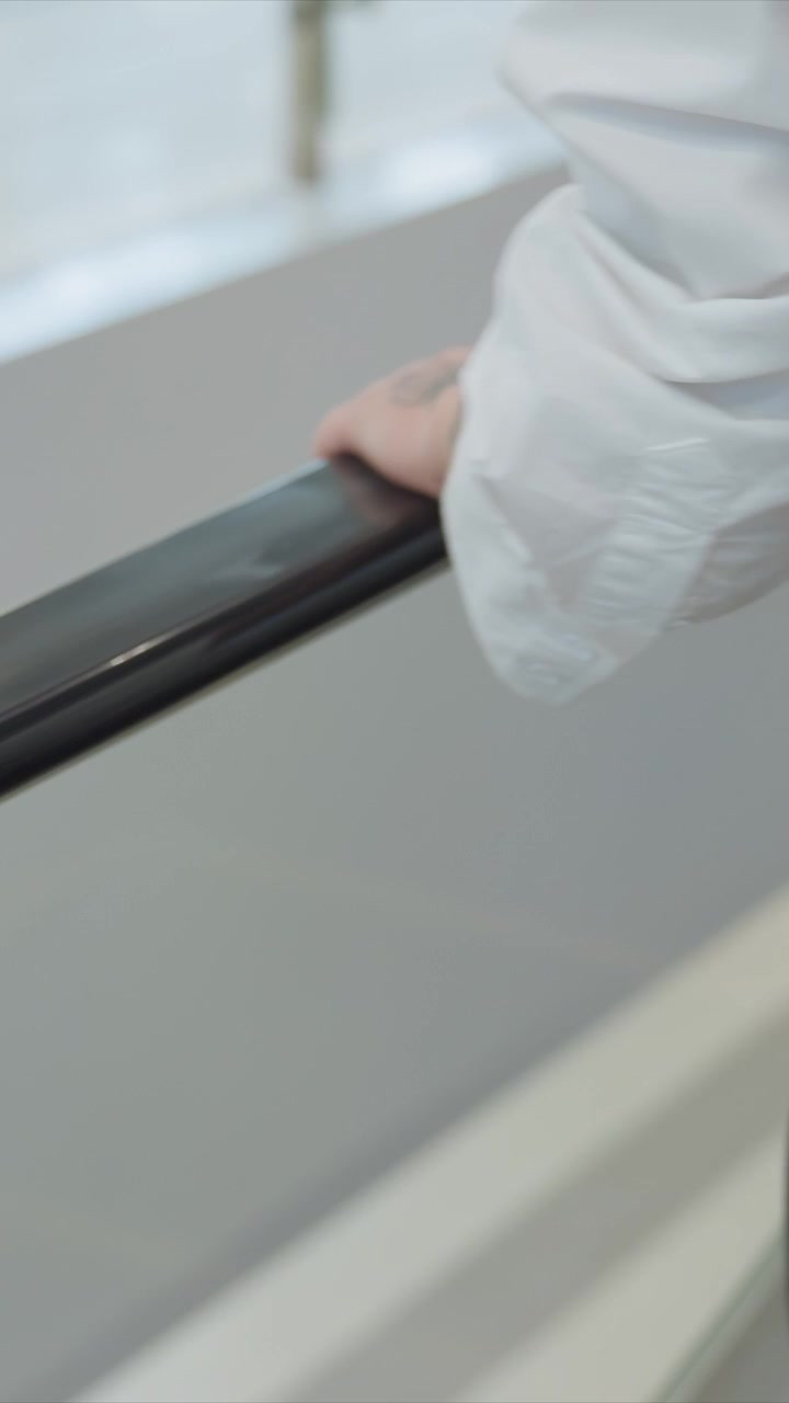 Primo piano di una persona vestita di bianco. La mano e parte del corpo della persona sono visibili mentre afferra un oggetto. L'illuminazione soffusa crea sottili riflessi sulle superfici lucide.