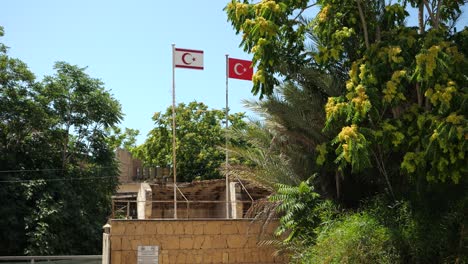 Two-Flagpoles-Holding-The-Turkish-Flag-Behind-Wall-Surrounded-by-Trees