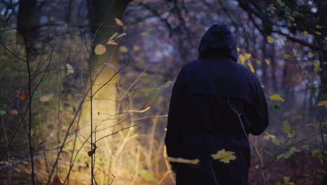 a man in a hood with a flashlight in his hand walks through a dark forest search for a man