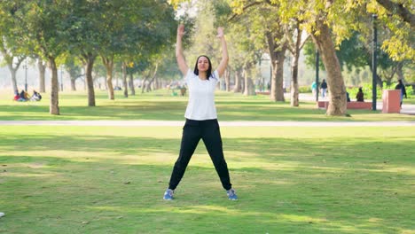 indian woman doing jumping jacks exercise in a park in morning