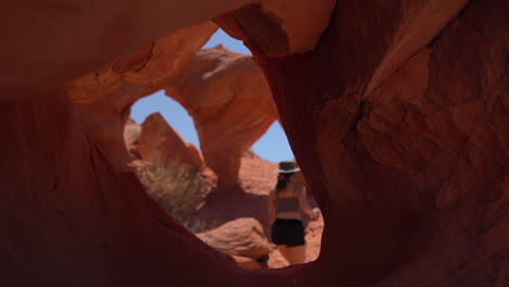 Young-Woman-Walking-Between-Strange-Natural-Arches,-Red-Sandstone-Rock-Formation-in-Valley-of-Fire-State-Park,-Nevada-USA