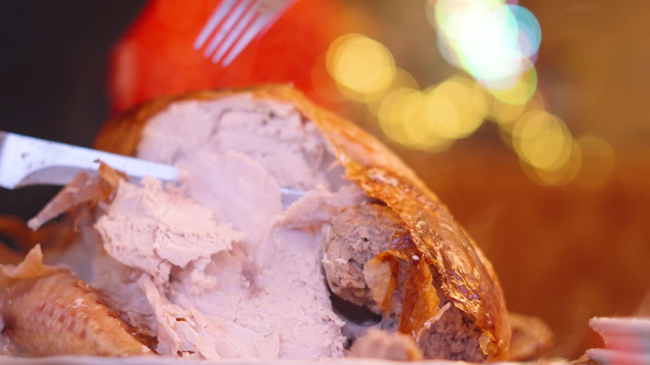 전통적인 크리스마스 칠면조 로스트가 날카로운 칼과 고기로 조각되어 있으며, xmas 조명이 배경으로 켜져 있으며, 느린 동작 증기가 상승하고 있습니다.