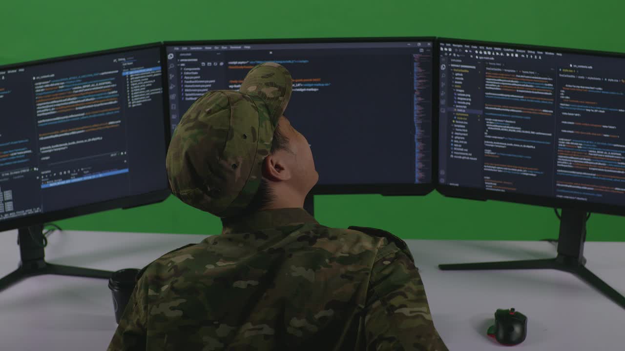 Back View Of Asian Man Soldier Developer Having Backache While Write Code With Multiple Computer Screens In Green Screen Studio