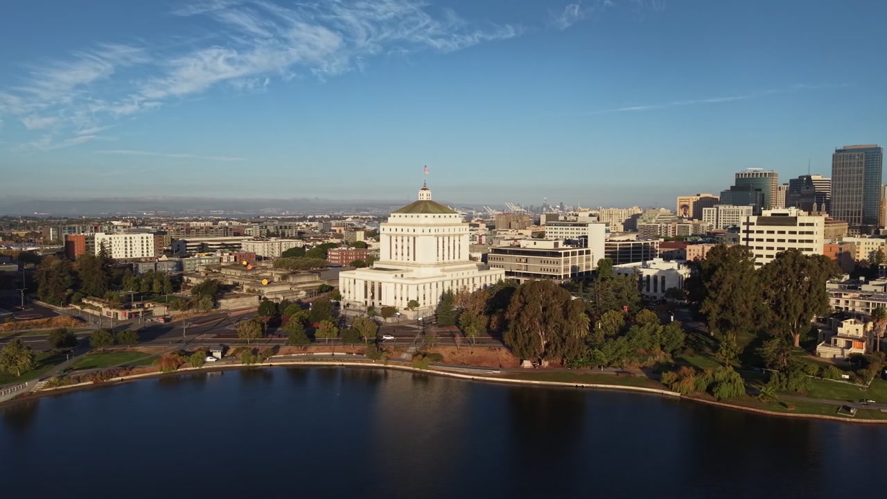 Veduta aerea mattutina che sorvola il Lago Merritt verso il tribunale della contea di Alameda con lo skyline del centro di Oakland sullo sfondo in una giornata limpida con cieli azzurri. Ripresa panoramica con drone.