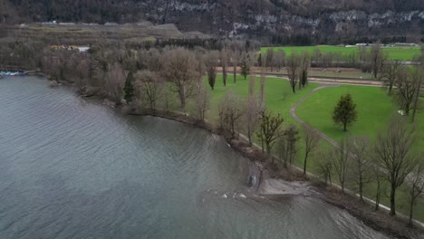 Windy-waves-slowly-bounce-on-grey-shoreline-banks-of-Lake-Walen-with-leafless-trees