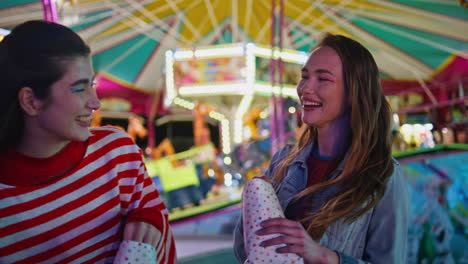 happy teenagers sharing secrets at illuminated carousel. cheerful friends gossip