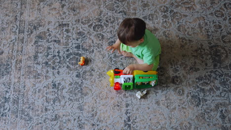 one year old toddler sitting on the carpet in the room. dark-haired boy plays with the toy train. top view.
