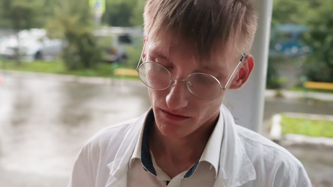 Young man in white coat wearing glasses carefully observing object with magnifying glass during outdoor study, reflecting precision, curiosity, and scientific approach to detailed observation
