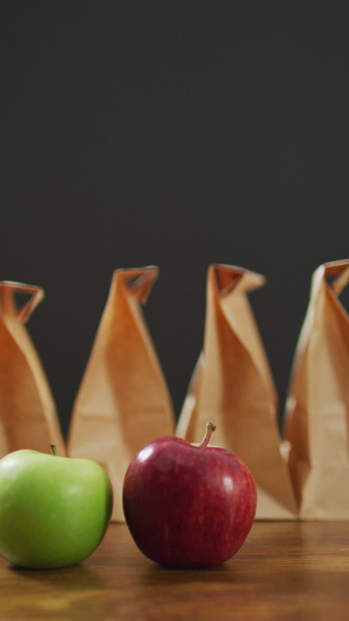 video vertical de manzana roja y verde con fila de almuerzos envasados en bolsas de papel y fondo gris