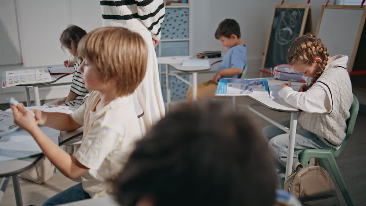 Children group doing test writing notebooks in school closeup. Teacher walking