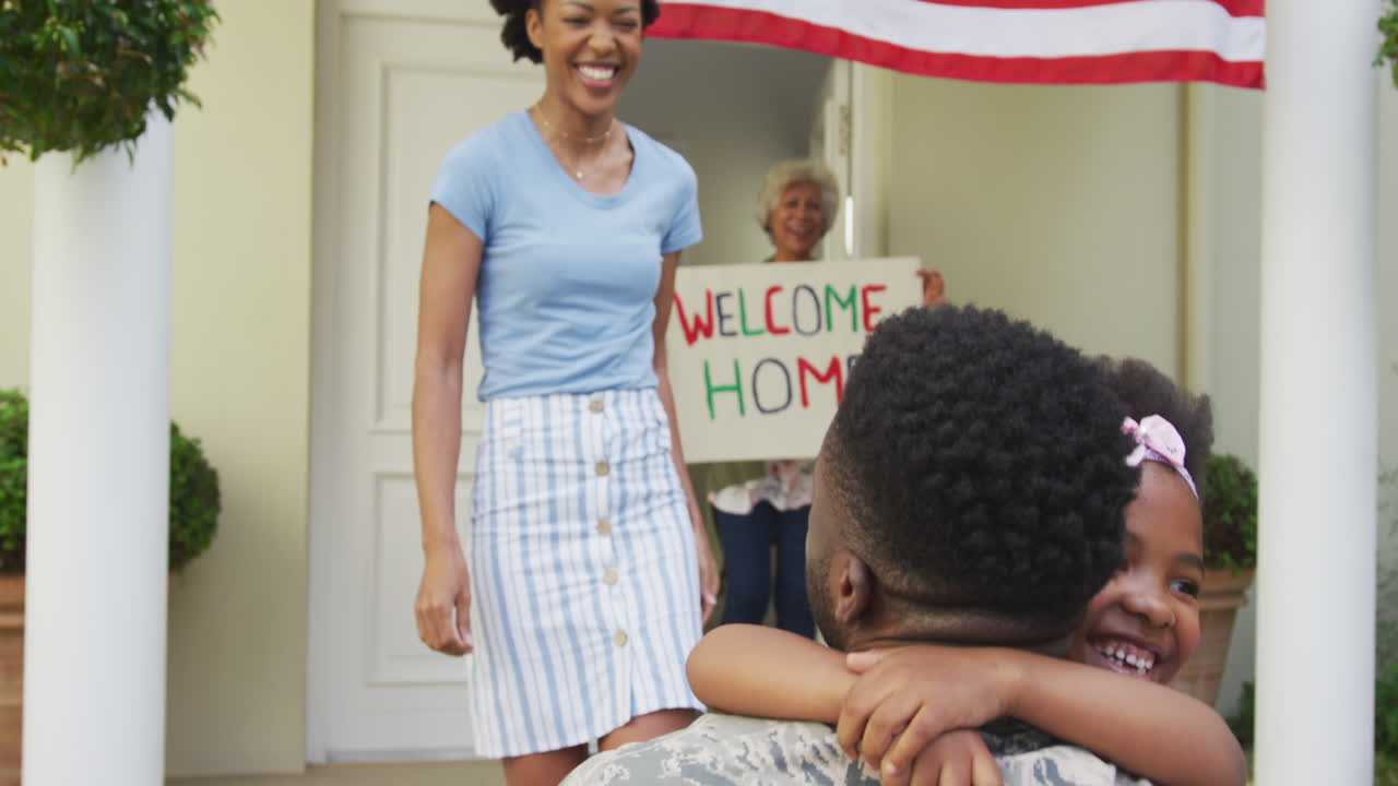soldado afroamericano abrazando a su sonriente esposa e hija con la bandera estadounidense