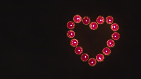 toma aérea de velas rojas encendidas en forma de corazón romántico sobre fondo negro 1