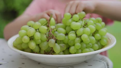 una niña pequeña está comiendo uvas verdes afuera durante el verano