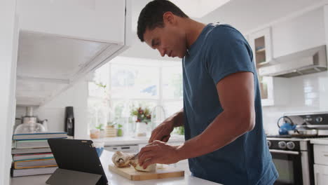 joven afroamericano preparando comida en la cocina usando una receta en una tableta, de cerca, vista lateral