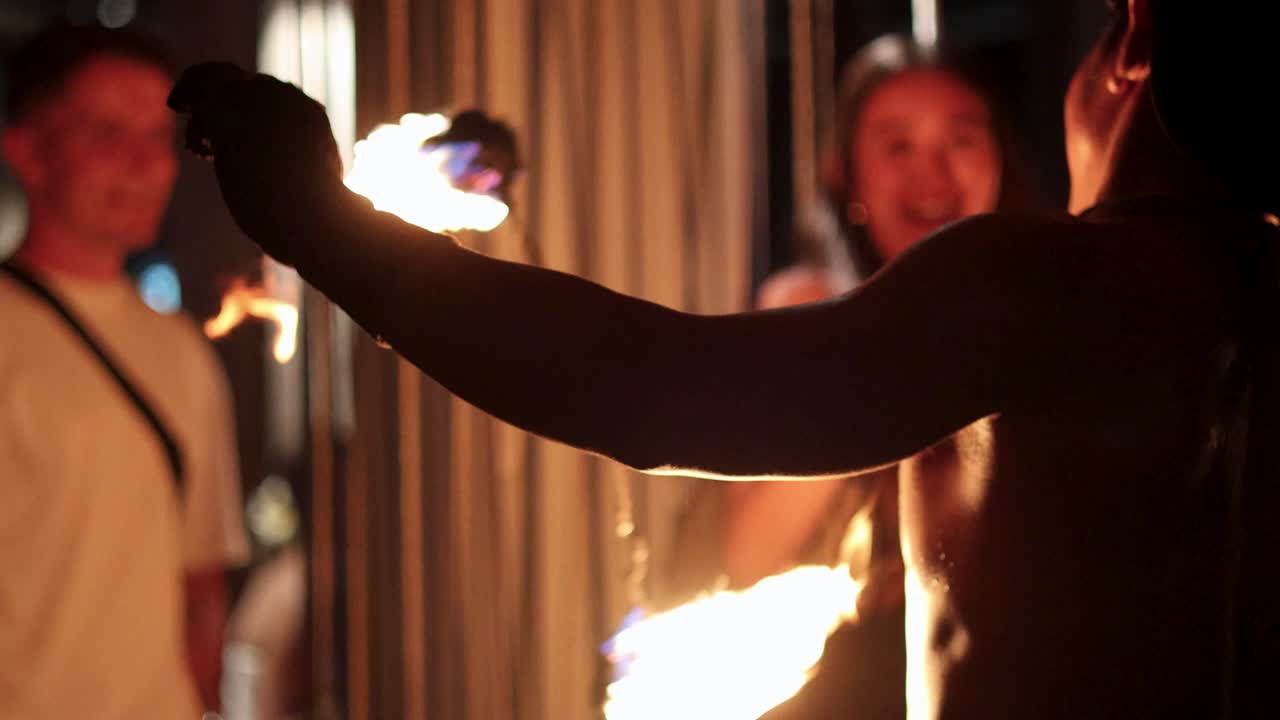 Shirtless performer spinning fire before an audience