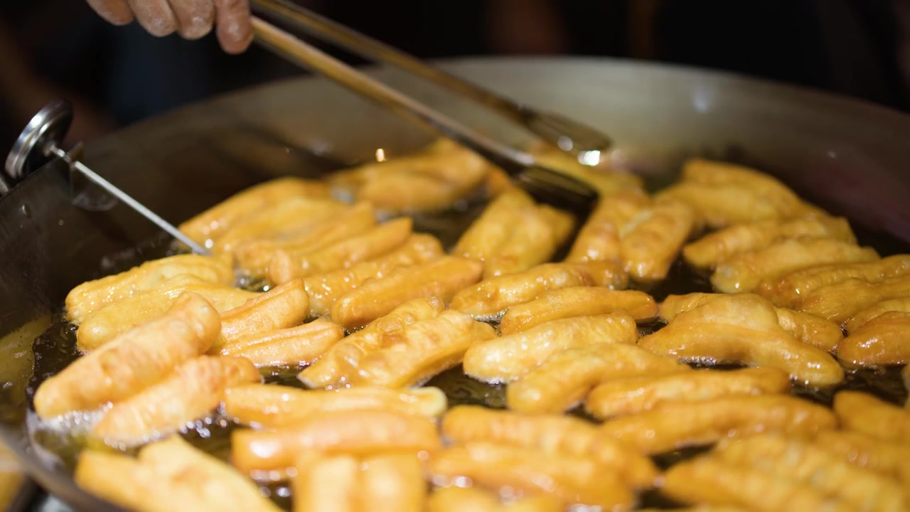 Gros plan sur des bâtonnets de pâte dorés frits dans de l'huile chaude sur un marché de Bangkok