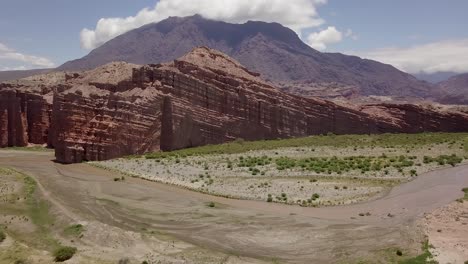 Amazing-scenic-aerial-shot-of-a-river,-riverbed,-rots-formations-and-a-mountain-range-on-a-sunny-day