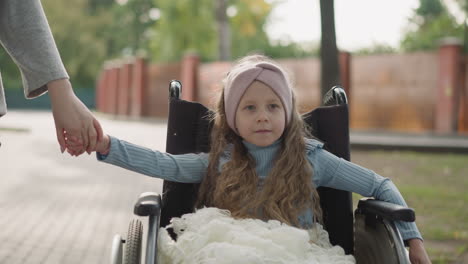 little girl spins wheel of wheelchair holding hand of mother