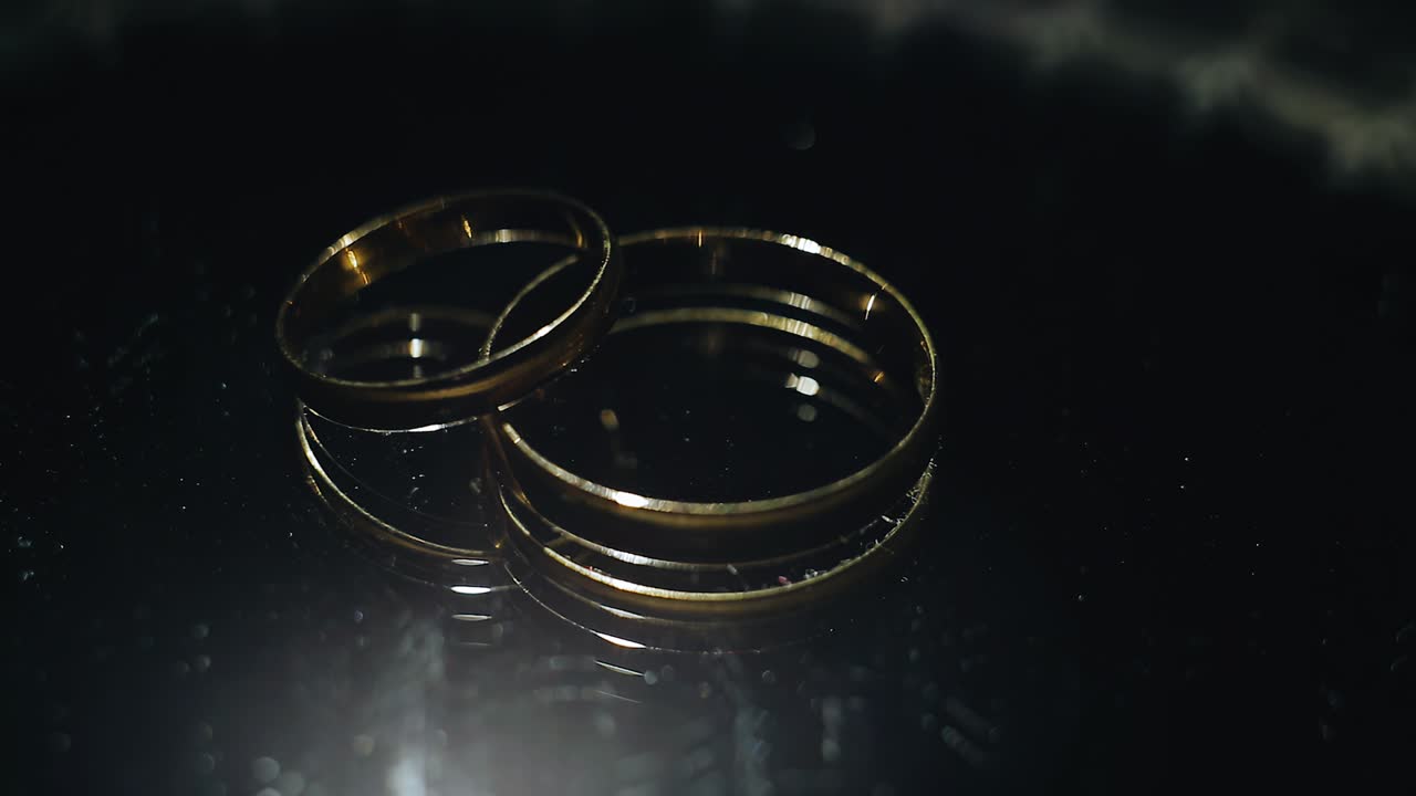 Beautiful gold wedding rings lie on a mirror surface. They are illuminated by dynamic light