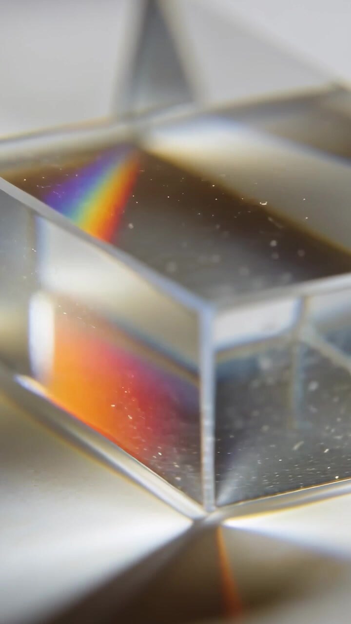 Vertical video: Light striking faceted prism making rainbows on table, showing geometry and dust