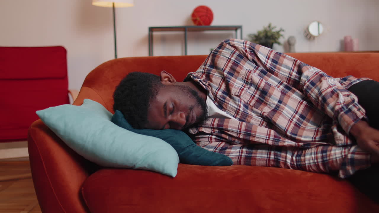 Homem afro-americano exausto adormecendo no sofá depois da festa, falta de energia, esgotamento