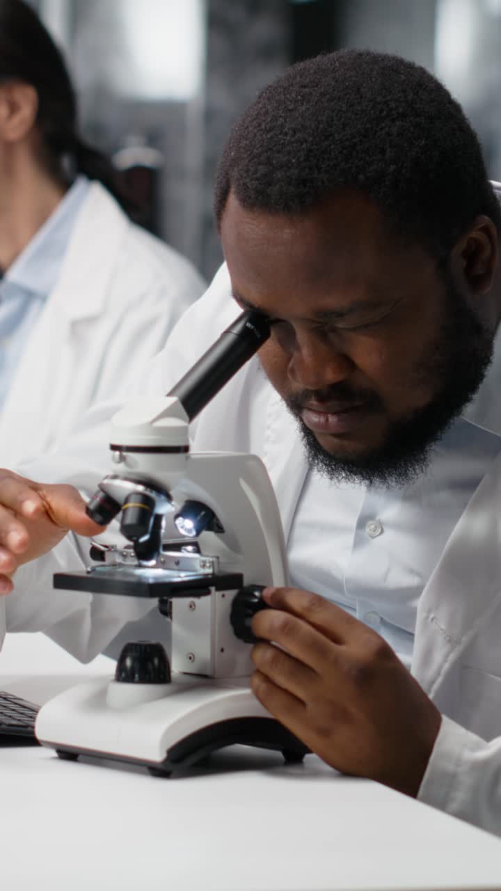 Video verticale: microbiologo clinico in laboratorio che usa il microscopio per la ricerca in patologia