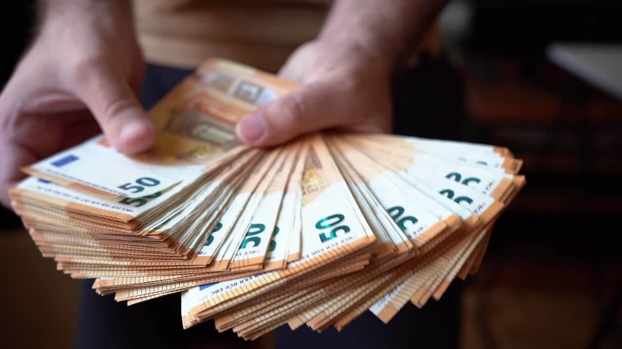 Hands of man showing a large pile of fifty euro bills.
