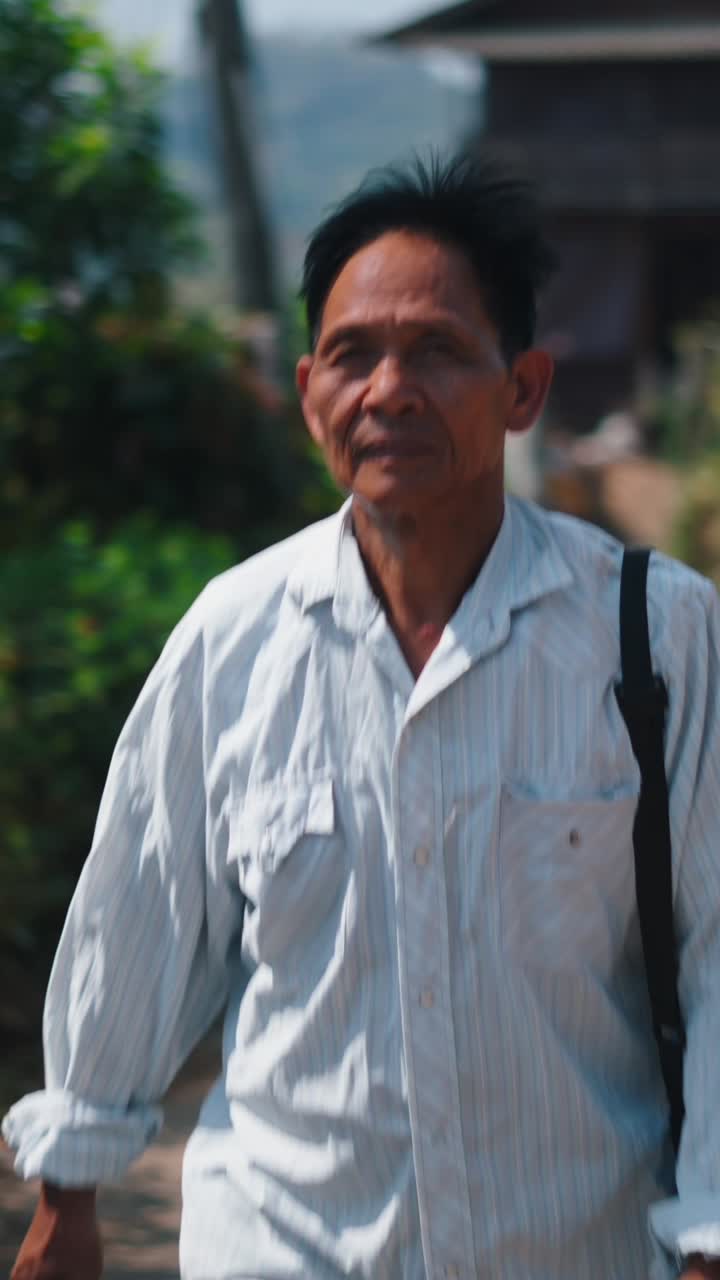 An elderly man walking down a rural street with a shoulder bag