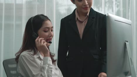 열광적인 아시아 여성 매니저가 새로운 고객 서비스 운영자를 가르치고 있습니다.