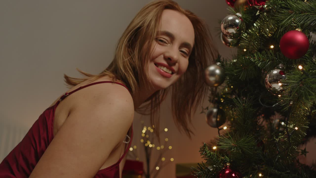 A fun young woman happily poses next to a decorated Christmas tree