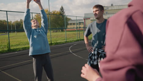 close-up partial view of individual in maroon hoodie passing volleyball to lady in cyan hoodie while man in background watches with hands on waist, reaching for ball in outdoor court