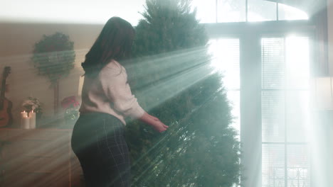 woman setting up christmas tree with sunbeams in home