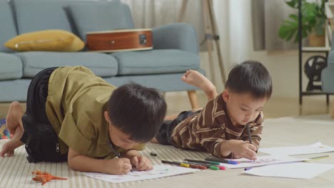 close up de niños asiáticos tendidos en el suelo en la habitación con ladrillo de juguete de plástico dibujando juntos en casa